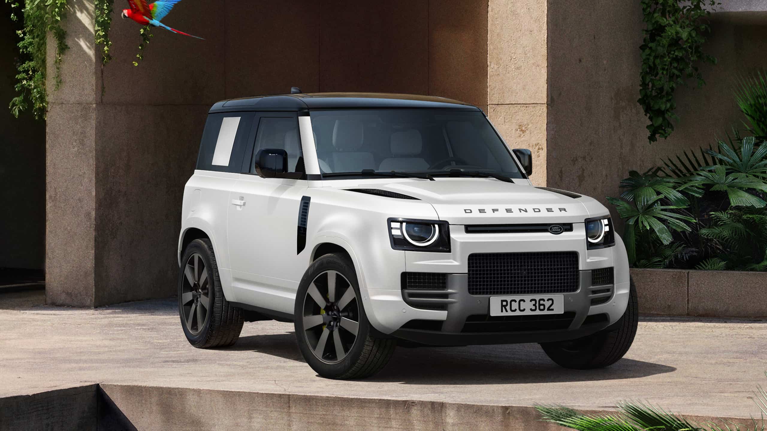 Widok z przodu na białego Land Rovera Defender stojący przed nowoczesną architekturą – SUV o charakterystycznym, prostokątnym nadwoziu i okrągłych reflektorach SUV-a marki Land Rover.