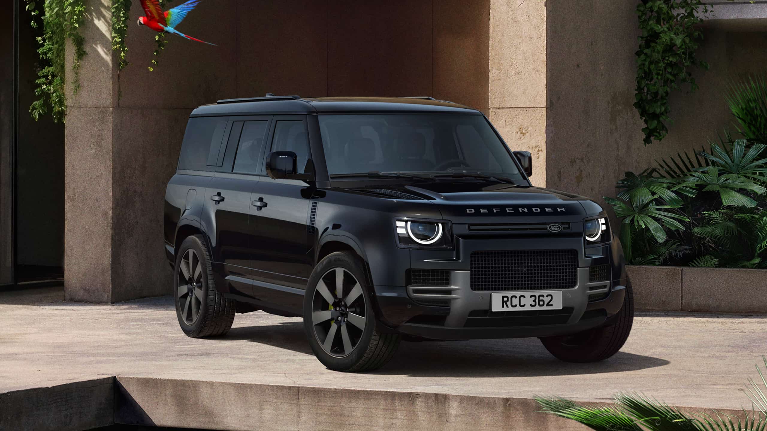 Czarny Land Rover Defender stojący przed nowoczesną architekturą — widok z przodu na SUV-a z charakterystycznymi okrągłymi reflektorami i wyraźnym napisem Defender na masce.
